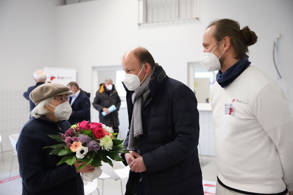 Landrat Martin Sailer (Mitte) und Lauritz Bahnemann, Ärztlicher Leiter des Impfzentrums in Gablingen, übergeben Kunigunde Haas aus Bobingen einen Blumenstrauß. Die Seniorin hat die 10.000ste Impfung im Landkreis Augsburg erhalten.